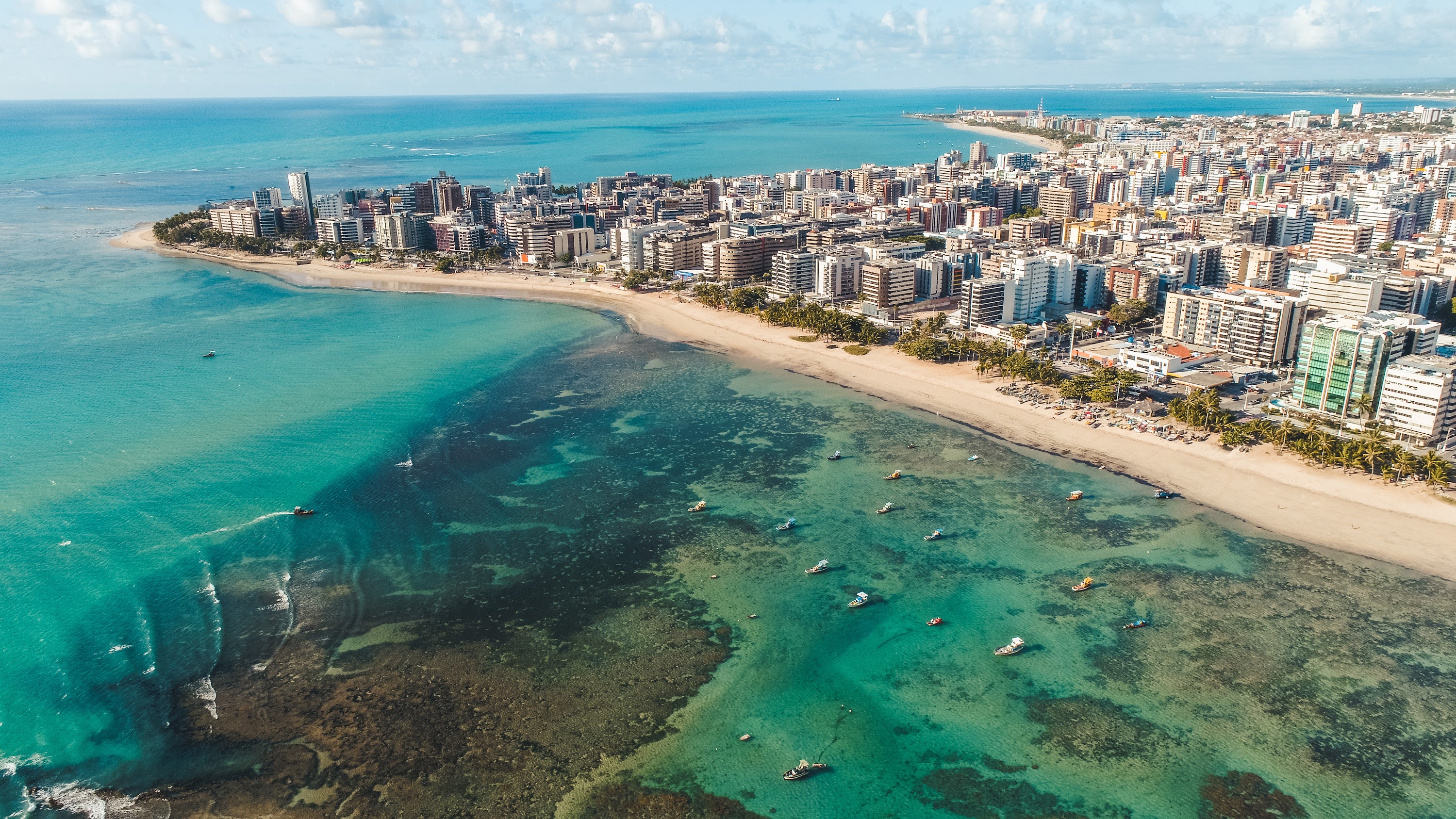 Vista aérea da costa de Maceió, com suas praias de águas cristalinas e edifícios modernos ao longo da orla.