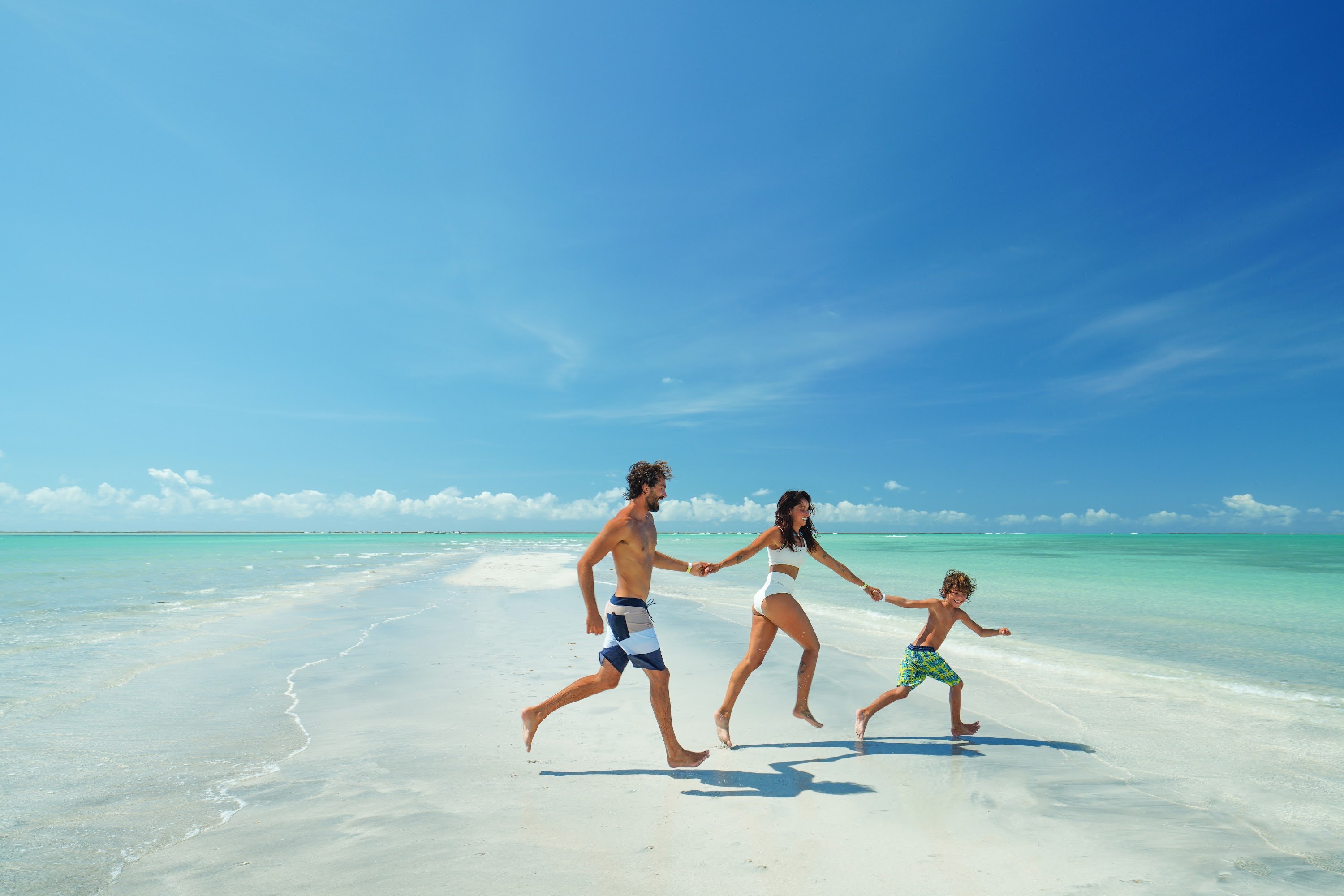 Família feliz correndo no cenário paradisíaco da Praia de Antunes, em Maragogi, Alagoas.