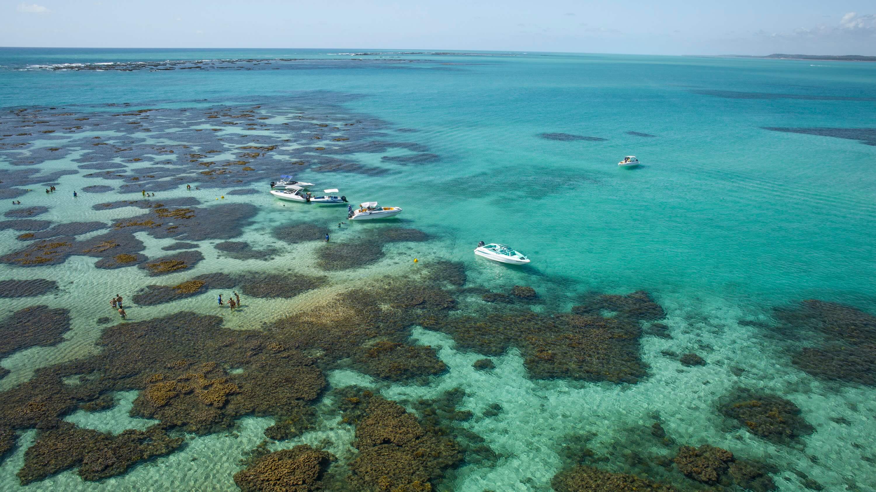 Vista aérea de pessoas tomando banho ao lado de lanchas de passeio, nas Galés de Maragogi da Croa de São Bento, em Alagoas.