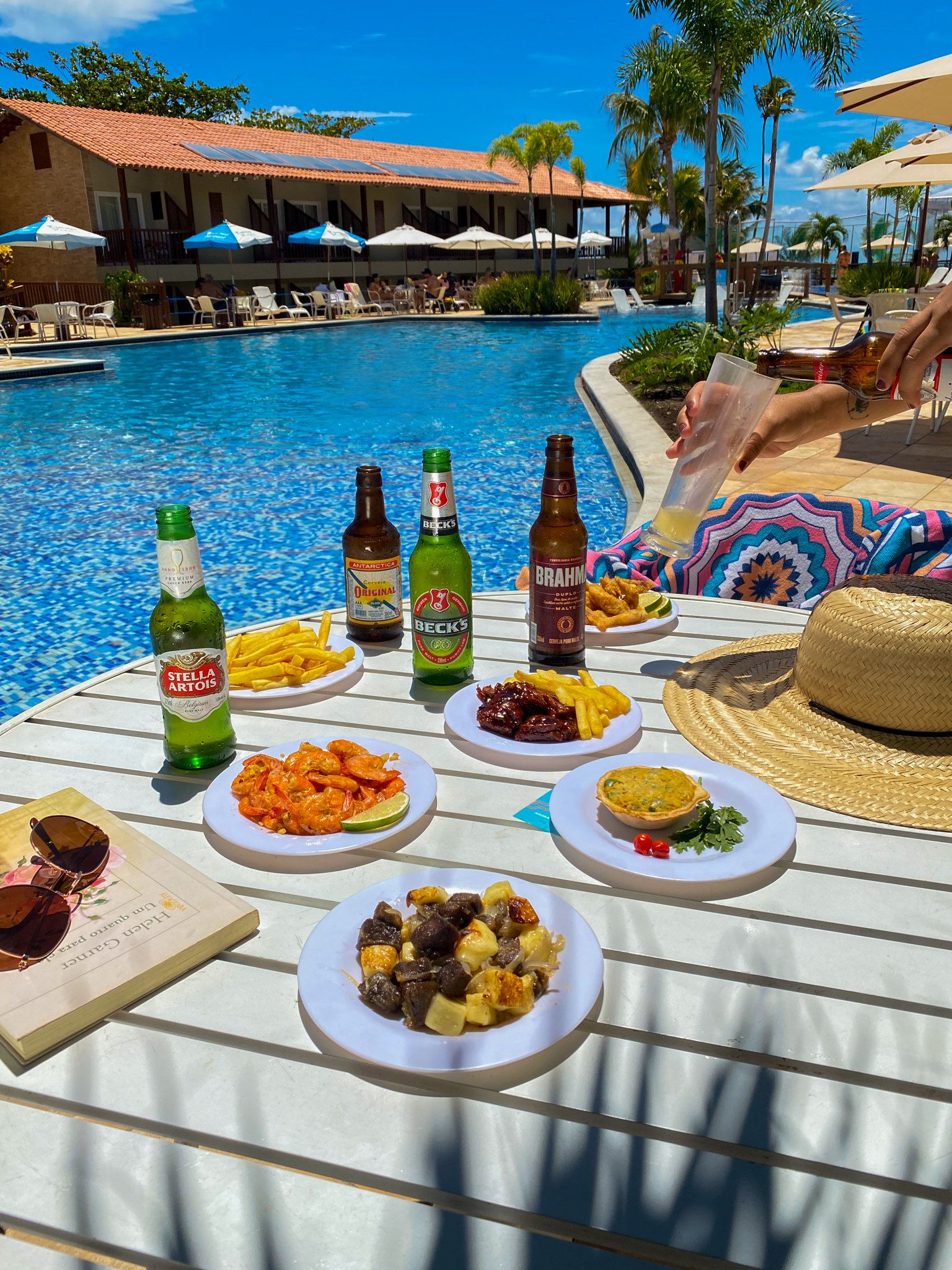 Mesa à beira da piscina do Salinas Maceió, com variedade de petiscos e cervejas.