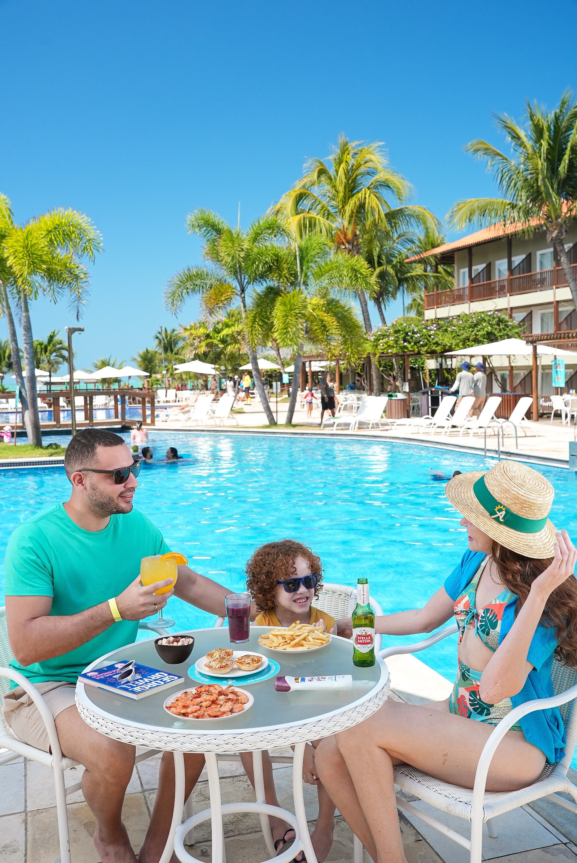 Família desfruta variedade de petiscos no Salinas Maceió All Inclusive Resort em mesa à beira da piscina.