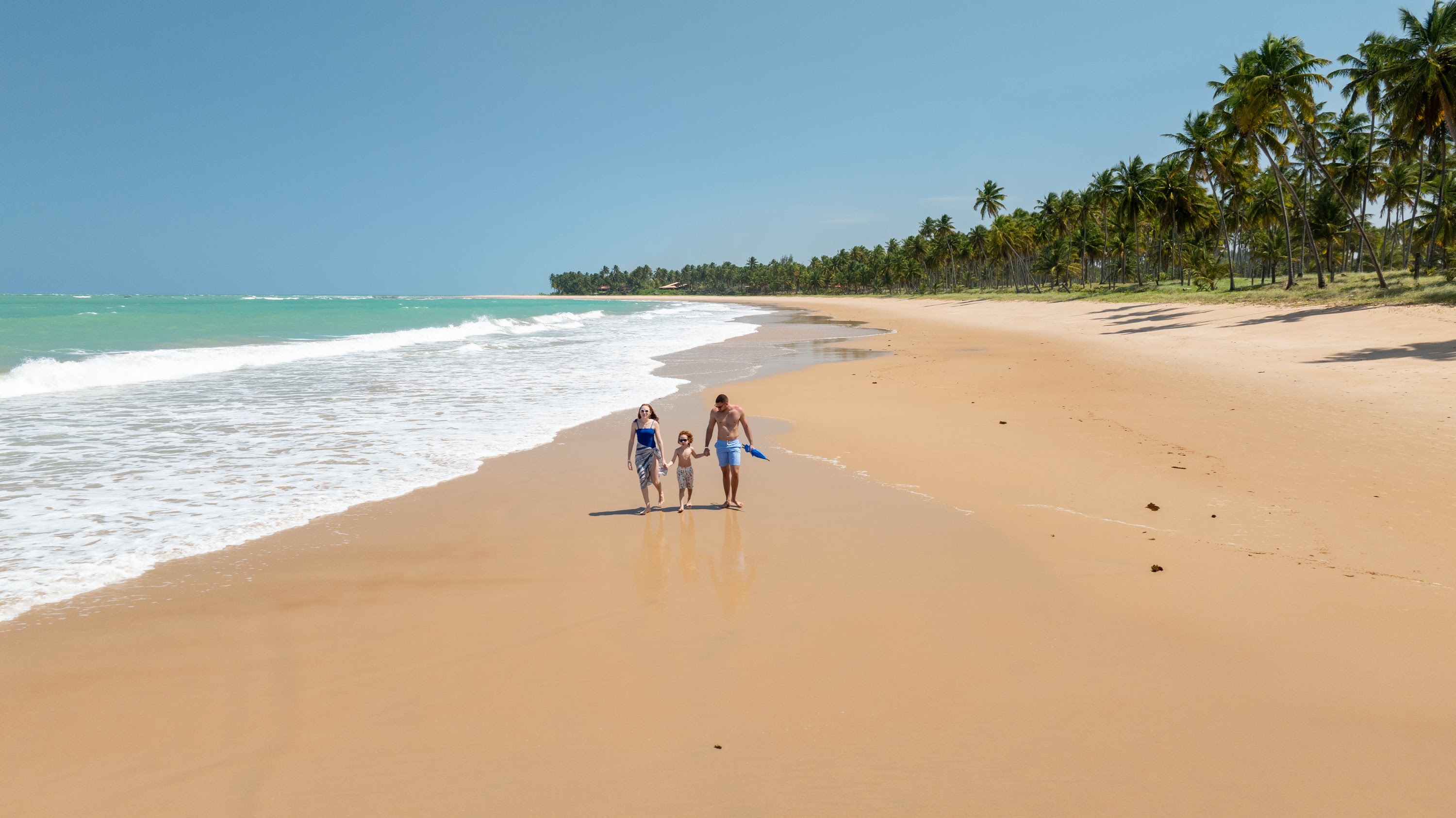 Família caminhando sobre a faixa de areia na Praia de Ipioca, onde fica o resort Salinas Maceió.