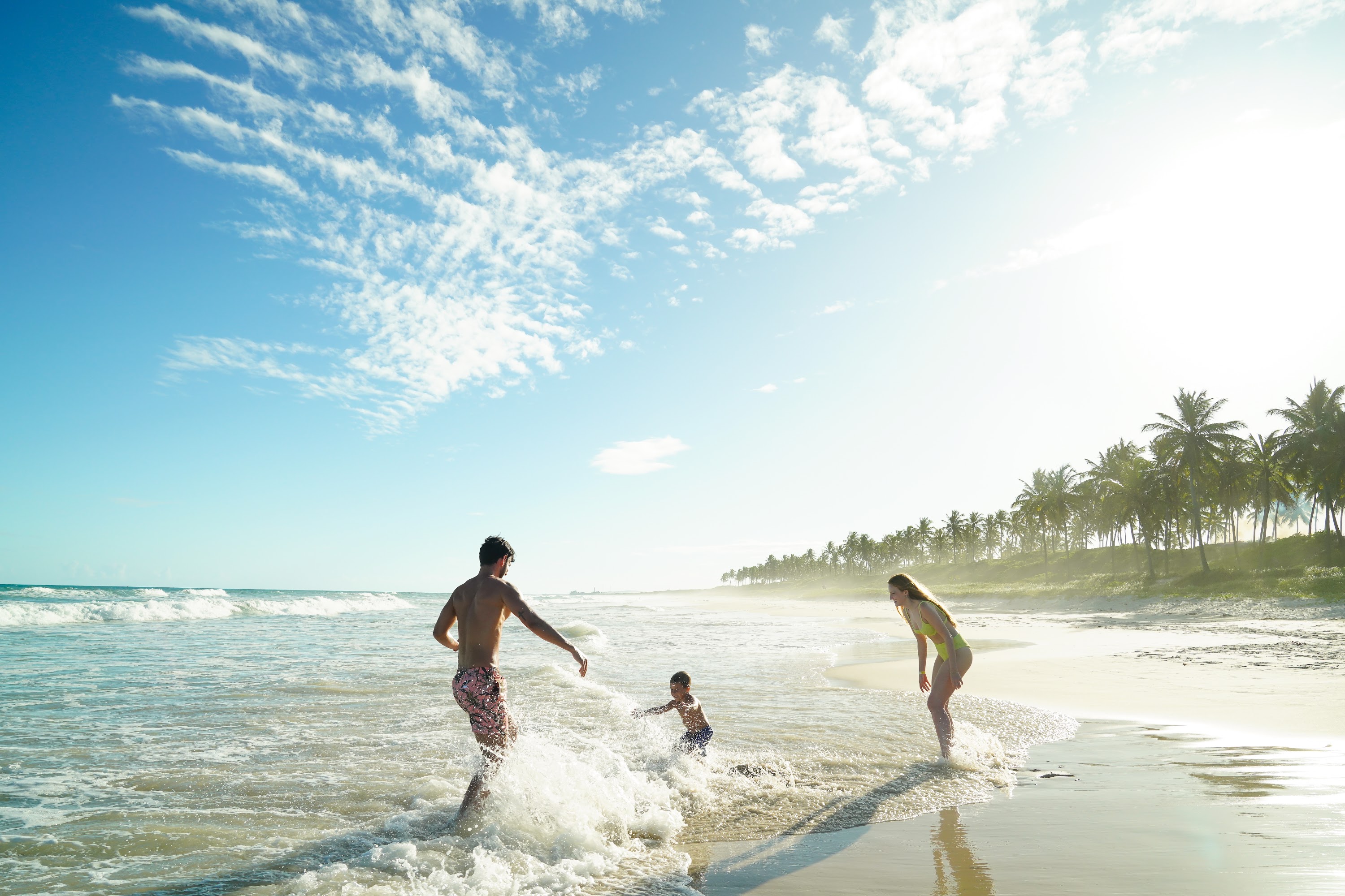 Família feliz brinca com as águas do mar na Praia de Ipioca, onde está localizado o Salinas Maceió All Inclusive Resort.