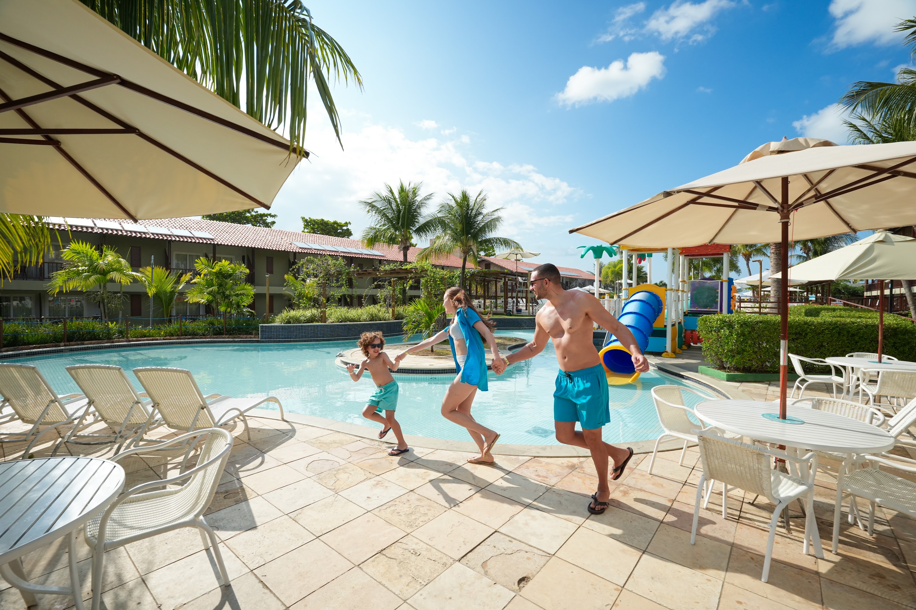 Família feliz correndo ao lado da piscina infantil do Salinas Maceió, resort All Inclusive na Praia de Ipioca.