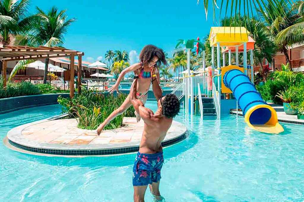 Um homem e uma criança se divertindo na água em um resort all inclusive, sorrindo e brincando juntos.