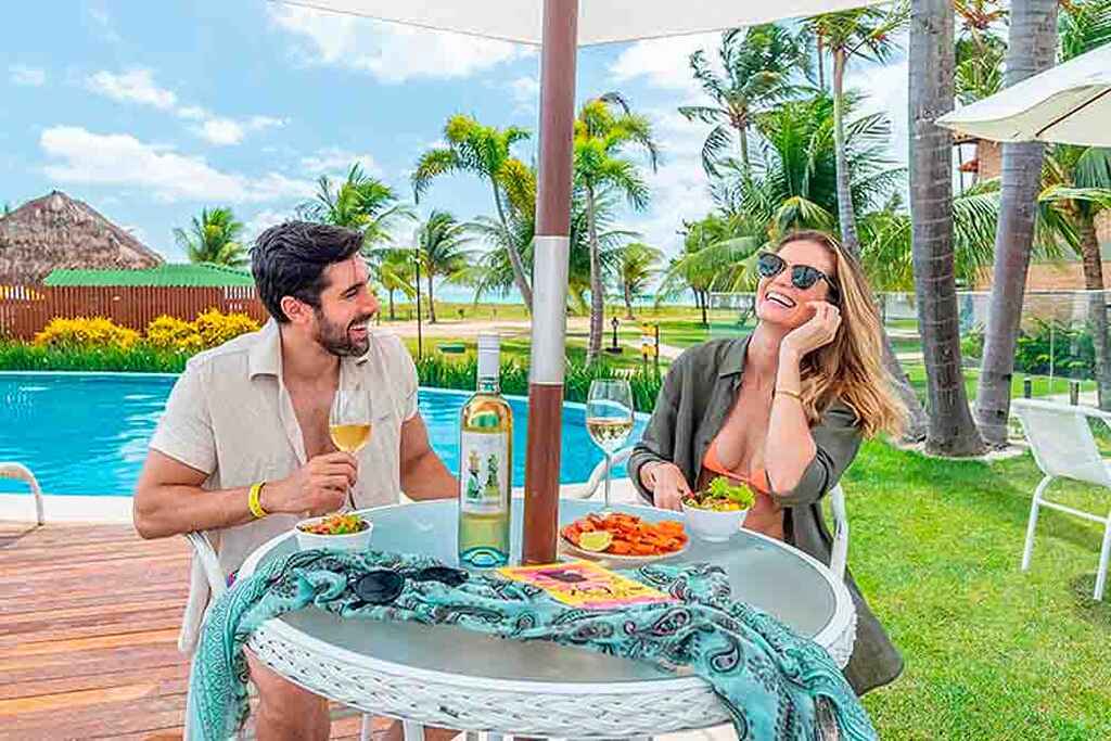 Um casal desfrutando de um almoço à beira da piscina, com um clima descontraído e alegre.