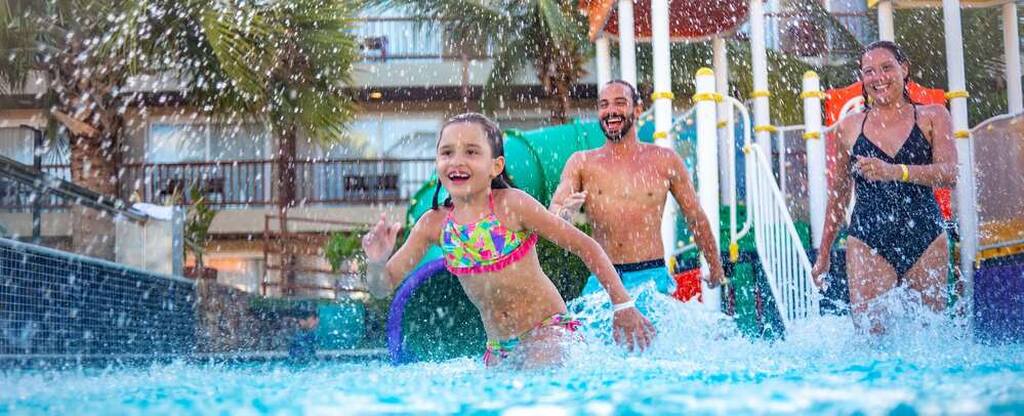 Família feliz brincando na piscina em um dia ensolarado na área de lazer do resort Salinas.