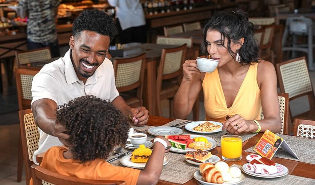 Família feliz curtindo café da manhã em restaurante, com risadas, comida deliciosa e momentos de confraternização, aproveitando a manhã com alegria.